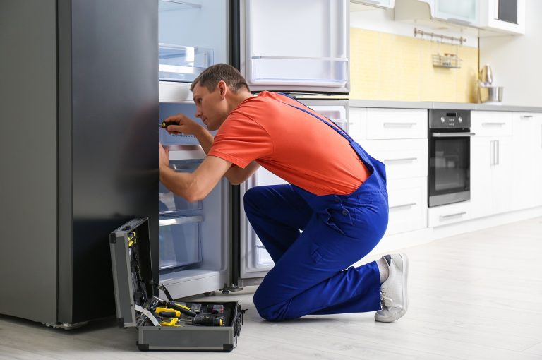 A man in overalls repairs an open refrigerator, showcasing local appliance repair services in action.