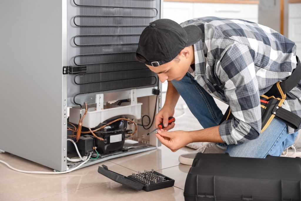 A man repairs a Marvel outdoor refrigerator in a kitchen, focused on fixing the appliance.