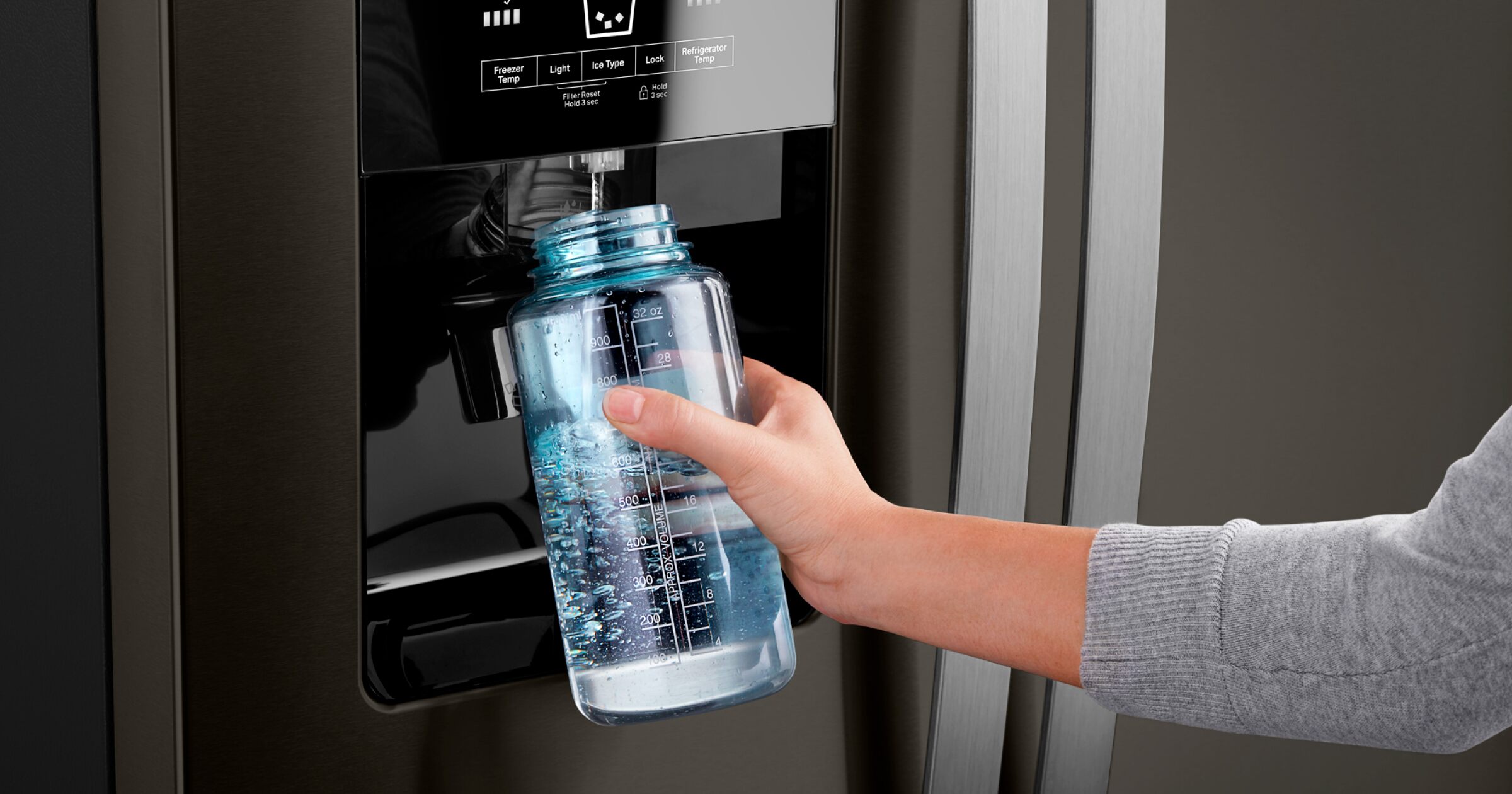 A person holds a bottle of water in front of an open refrigerator.