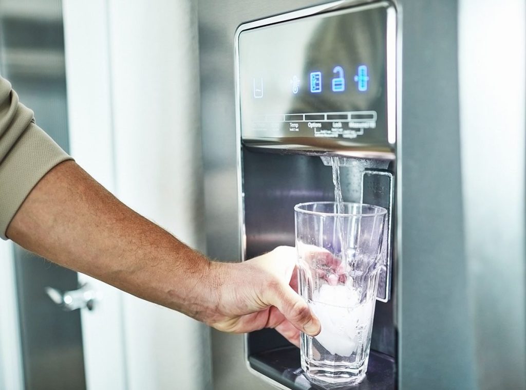 A person pours water from a dispenser into a clear glass.
