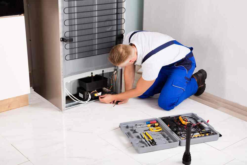A man conducting a refrigerator repair in a kitchen, focused on fixing the appliance.