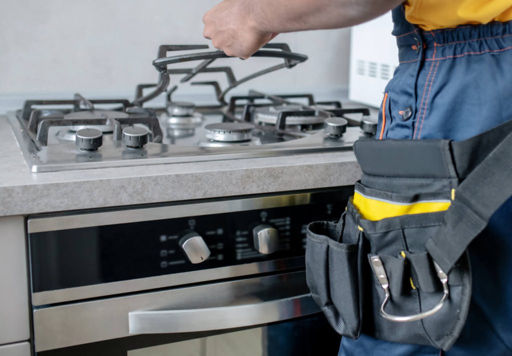 A man in a blue shirt and yellow vest holds a tool, preparing for stove repair.