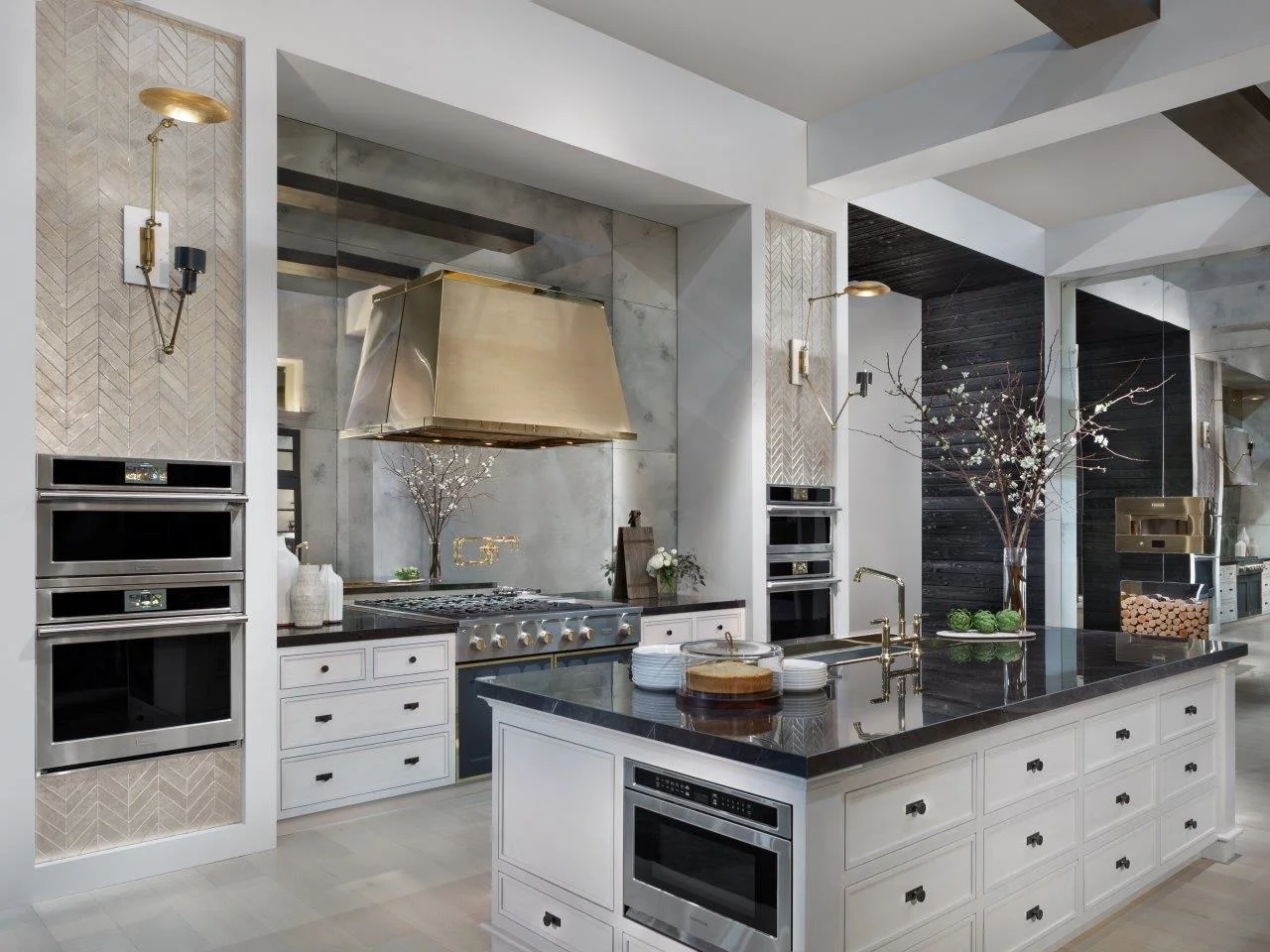 Luxurious kitchen with sleek white cabinetry, dark countertops, and a central island. Modern appliances, elegant lighting, and decorative branches add sophistication.