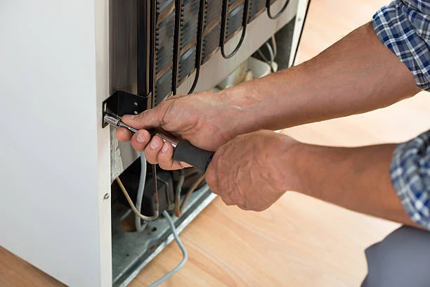A man is using a screwdriver to fix a refrigerator, demonstrating appliance repair skills.