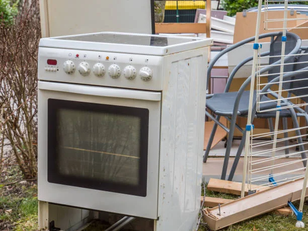 A white Electrolux stove placed in a yard among various other items, indicating appliance repair work in progress.

