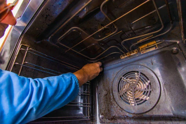 A man cleans a Viking oven using a fan, demonstrating effective kitchen maintenance techniques.