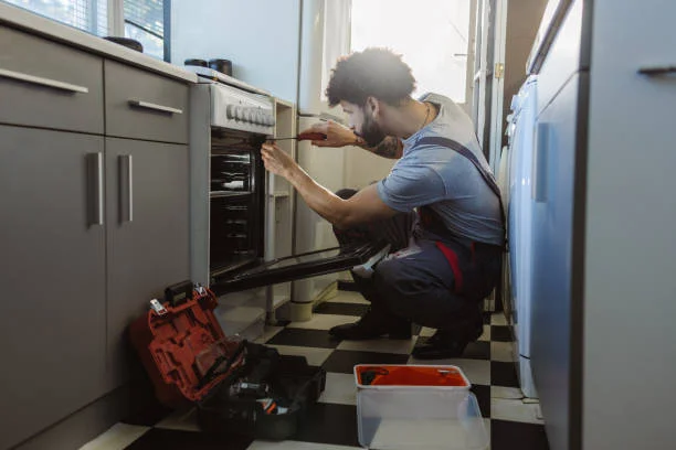 A man repairing a stove in a kitchen, focused on fixing the stove's internal components.